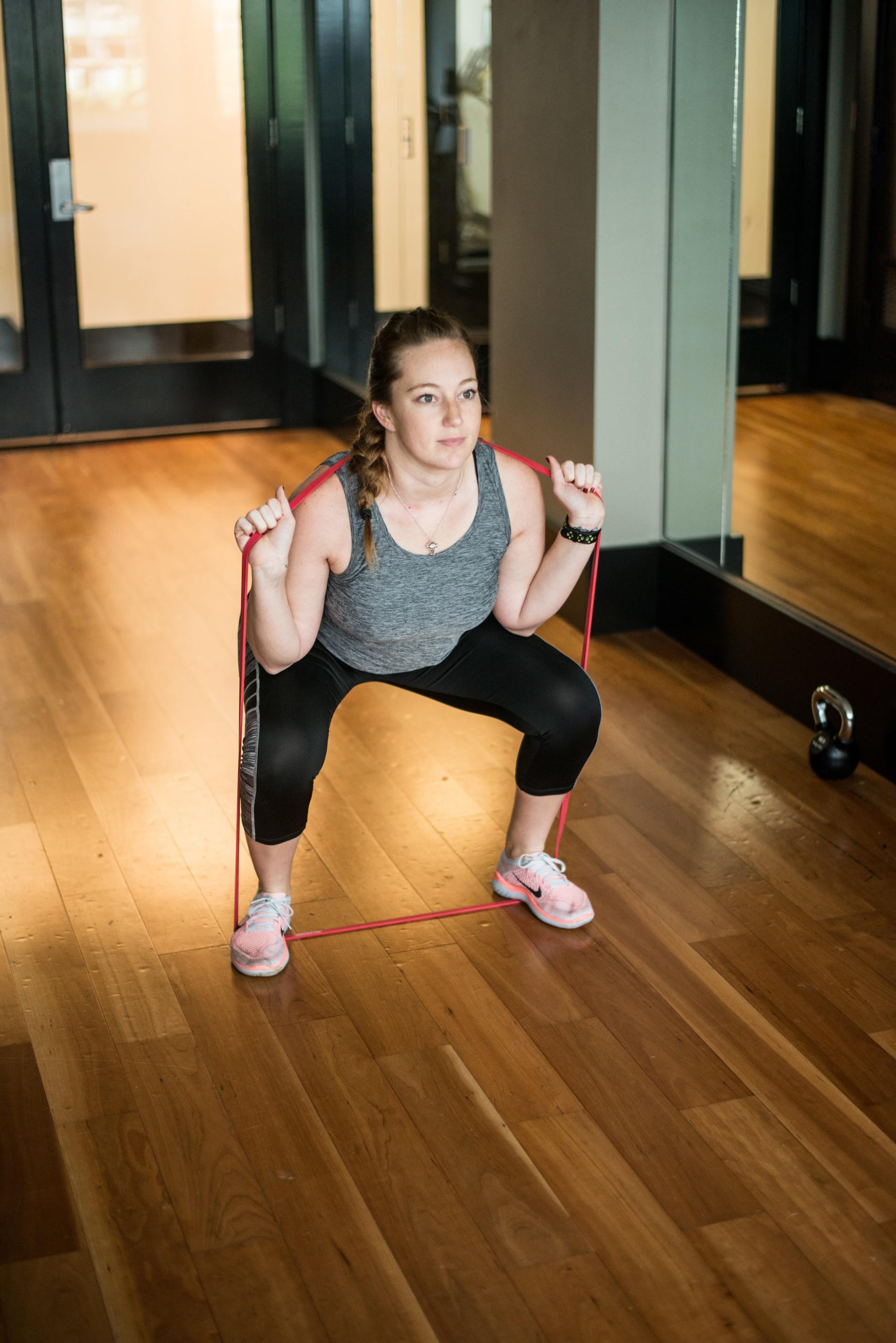 A woman is squatting with a resistance band in a gym.