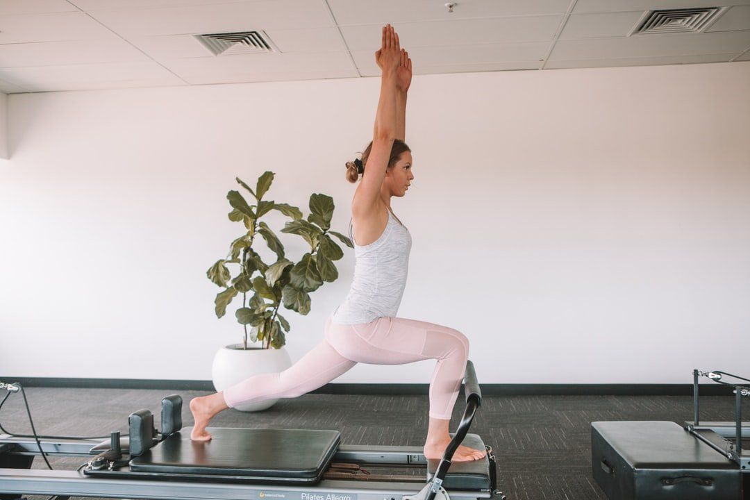 A woman is doing yoga on a pilates machine in a gym.