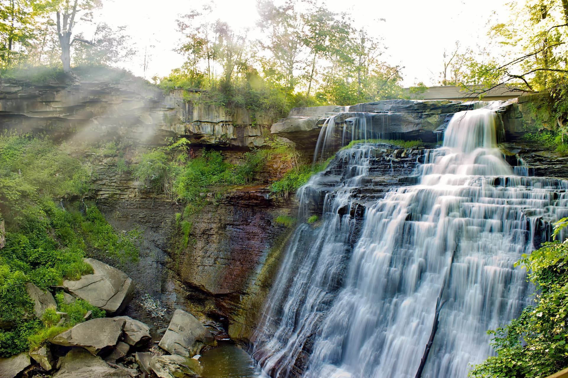 A waterfall is surrounded by trees and rocks in the middle of a forest.