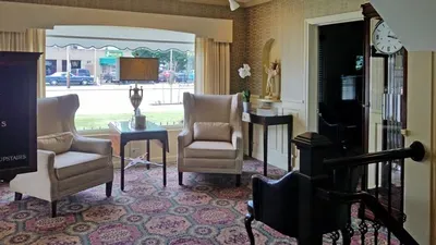 A living room with chairs , tables , a clock and a television.