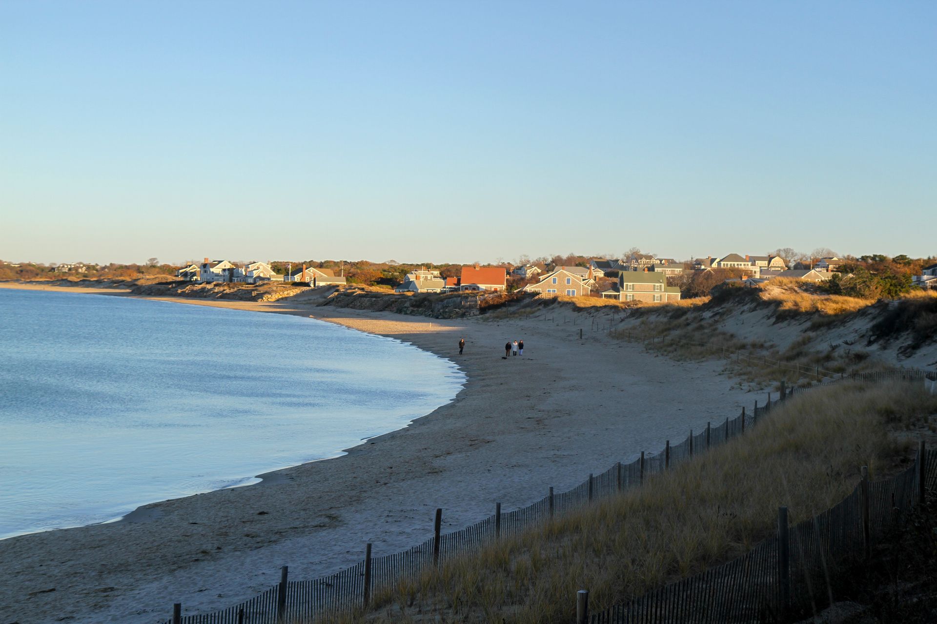 A beach with a fence and houses in the background