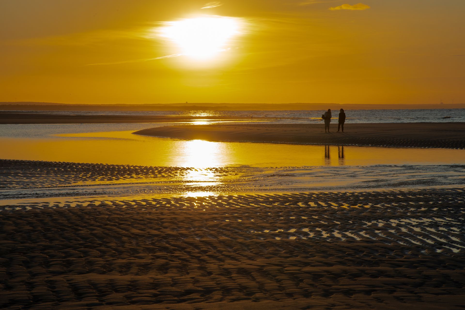 Two people are walking on the beach at sunset.