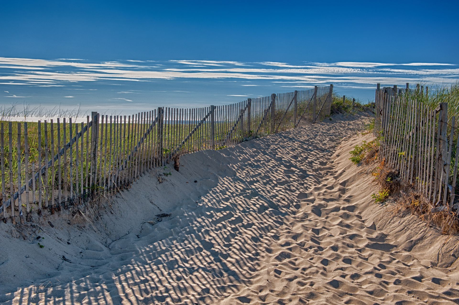 A sandy path leading to the beach with a wooden fence.