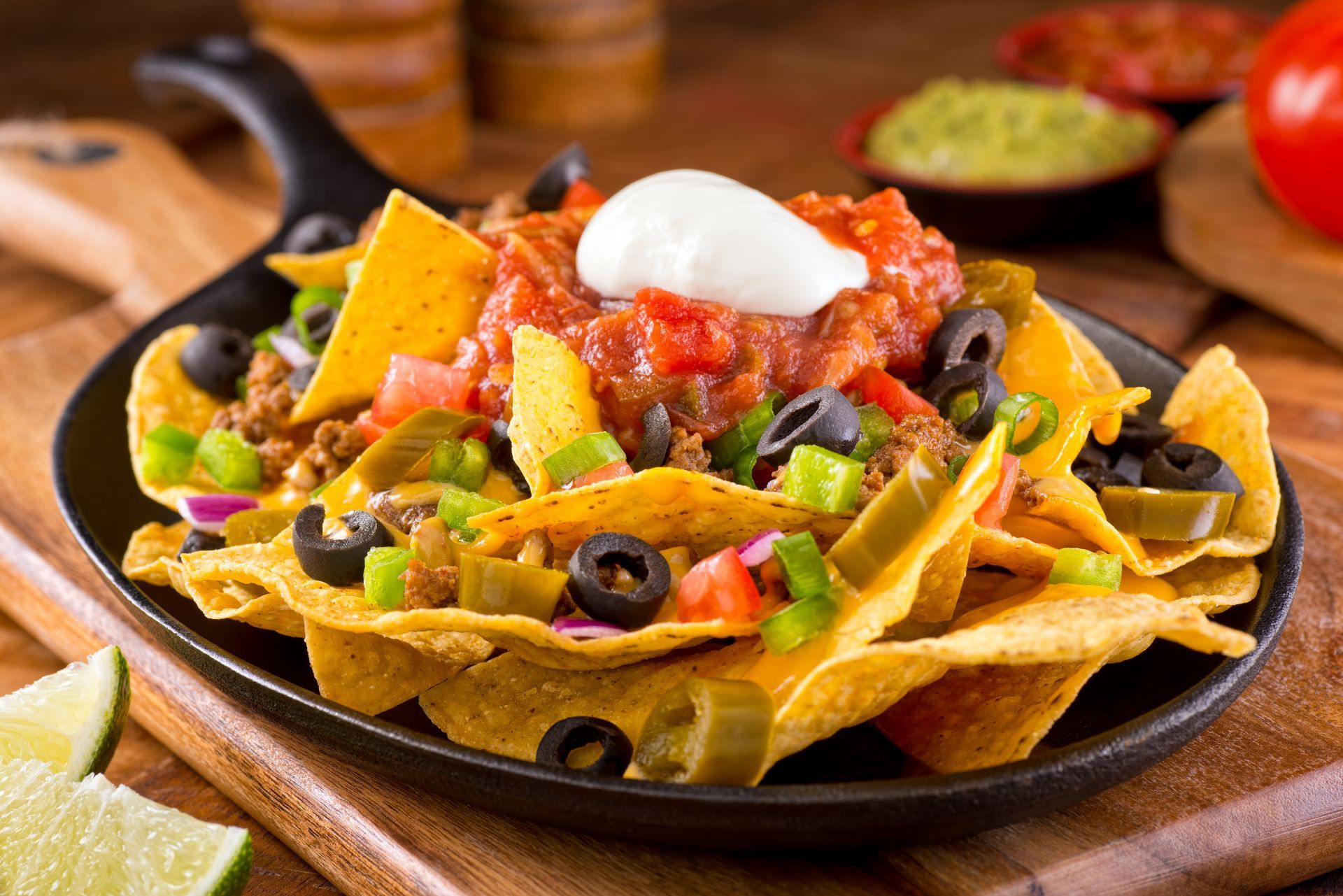 A pan filled with nachos with salsa , sour cream , olives , and meat.