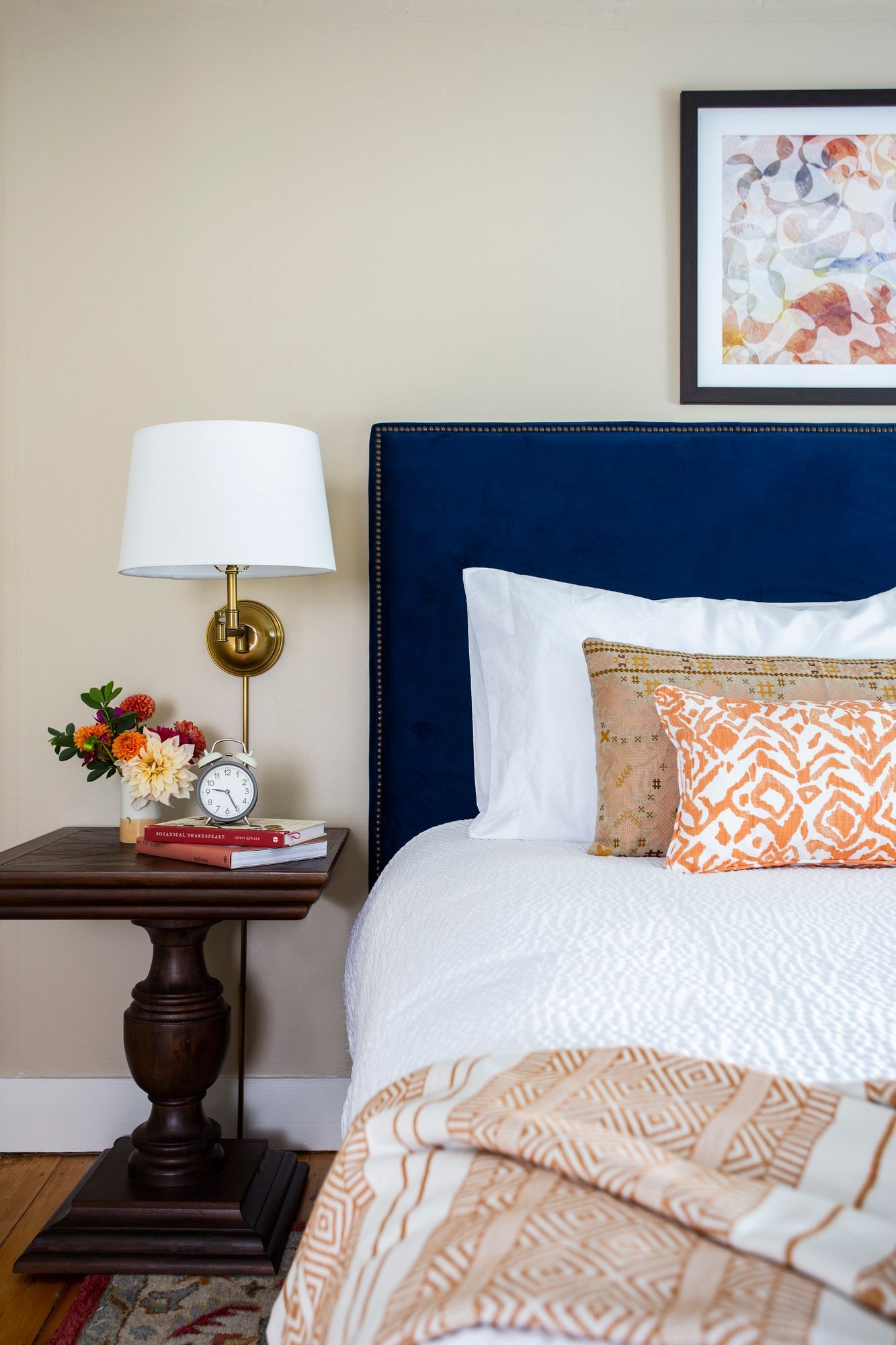 A bedroom with a bed , nightstand , lamp and picture on the wall.