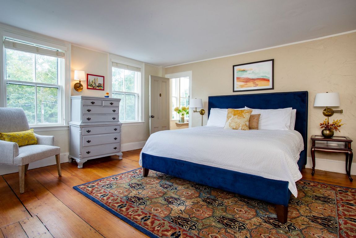 A bedroom with a king size bed , dresser , chair and rug.