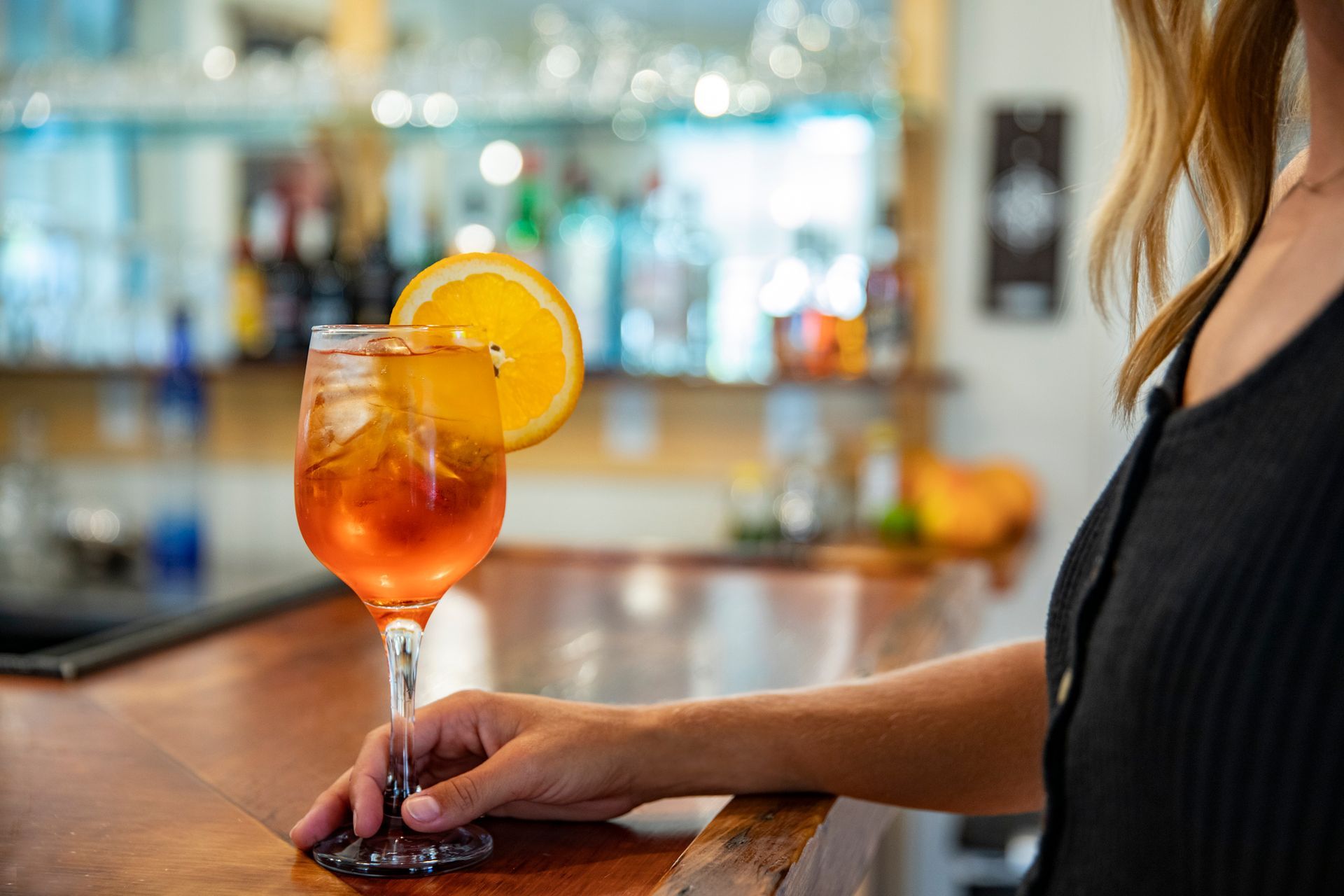 A woman is sitting at a bar holding a glass of orange juice.