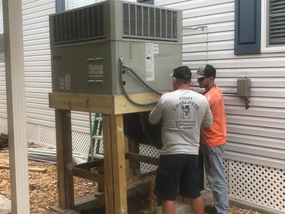 Two men are working on an air conditioner outside of a house.