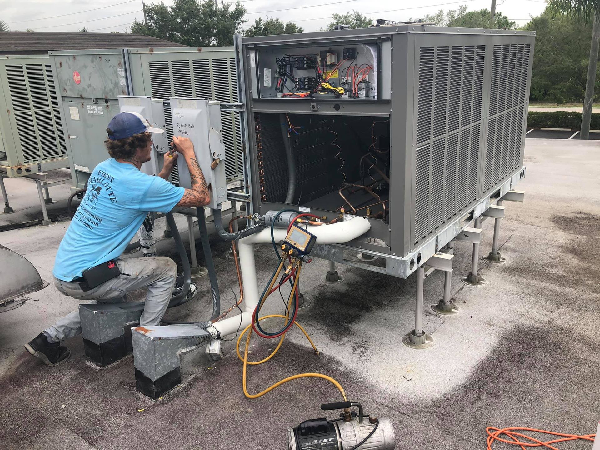 A man is working on an air conditioner on the roof of a building.