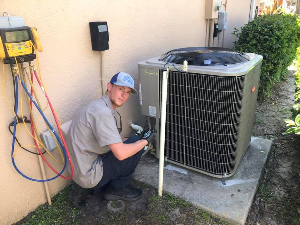 A man is kneeling down next to an air conditioner.