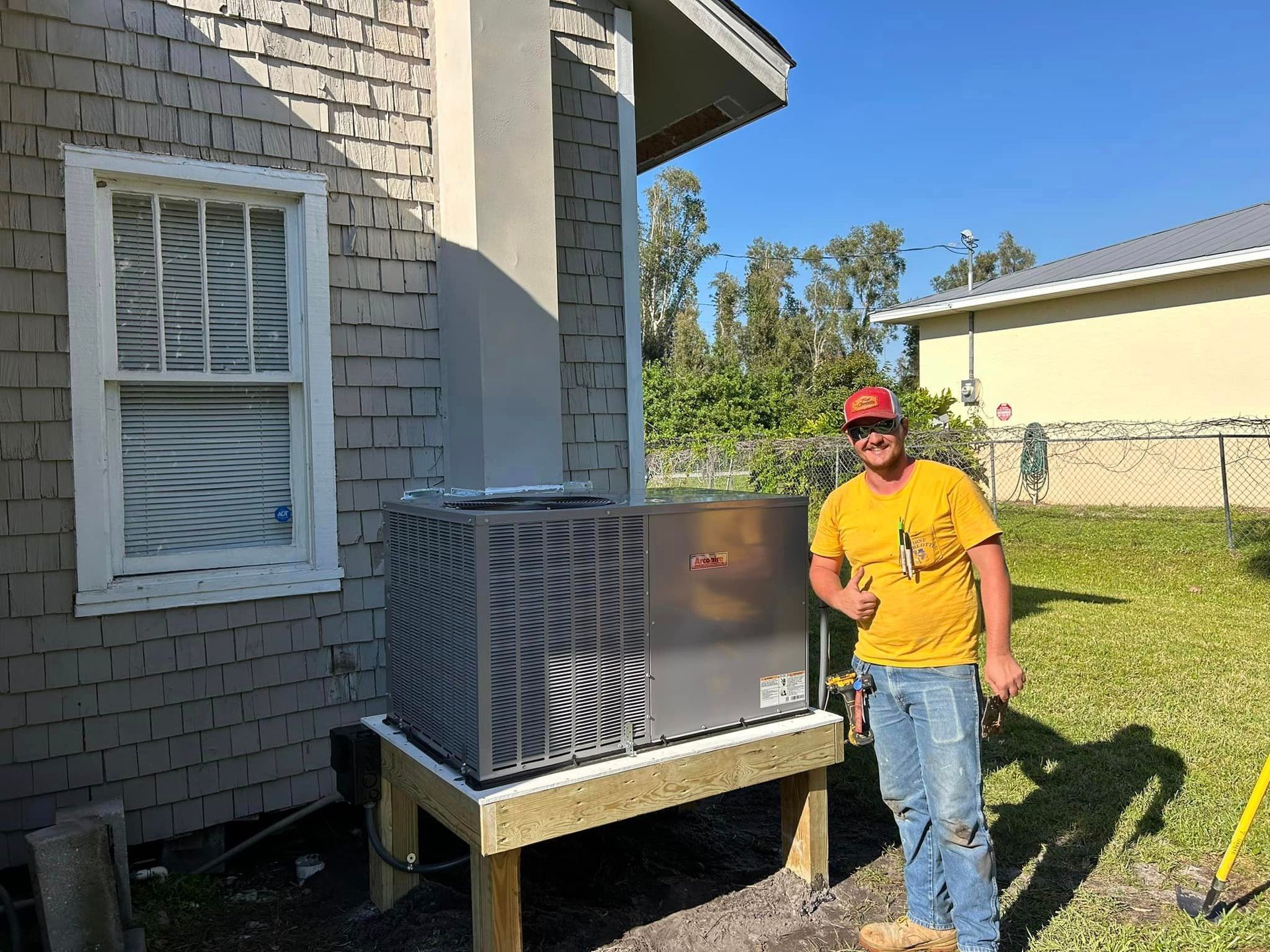 A man is standing in front of a house with an air conditioner.