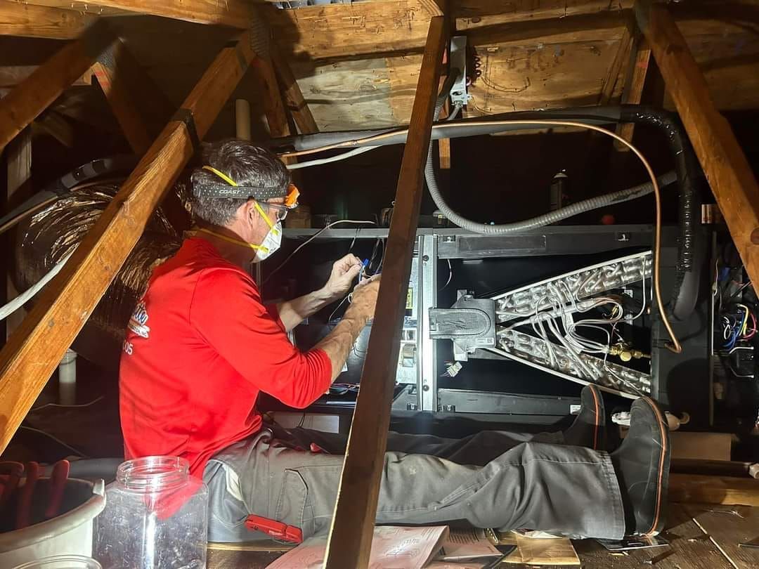 A man wearing a mask is working on a machine in an attic.