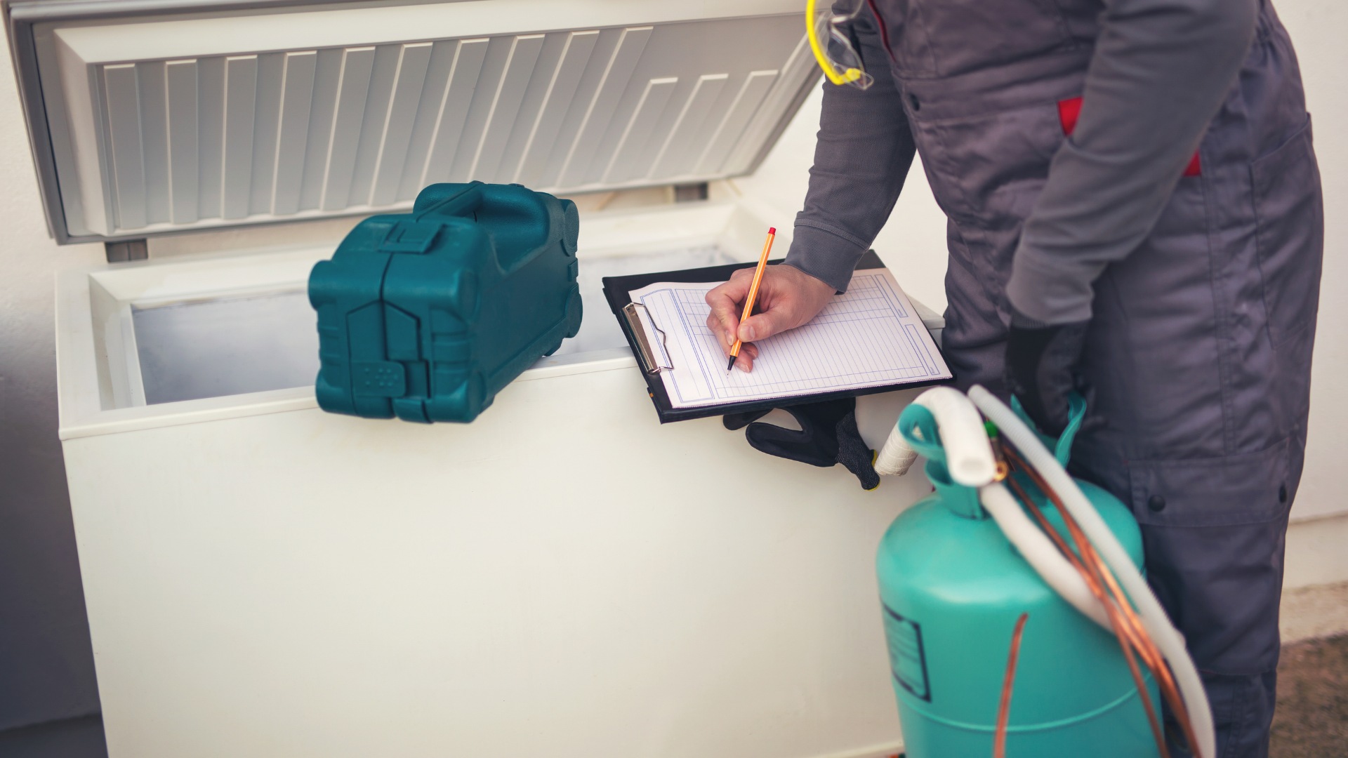 A man is writing on a clipboard in front of a freezer.