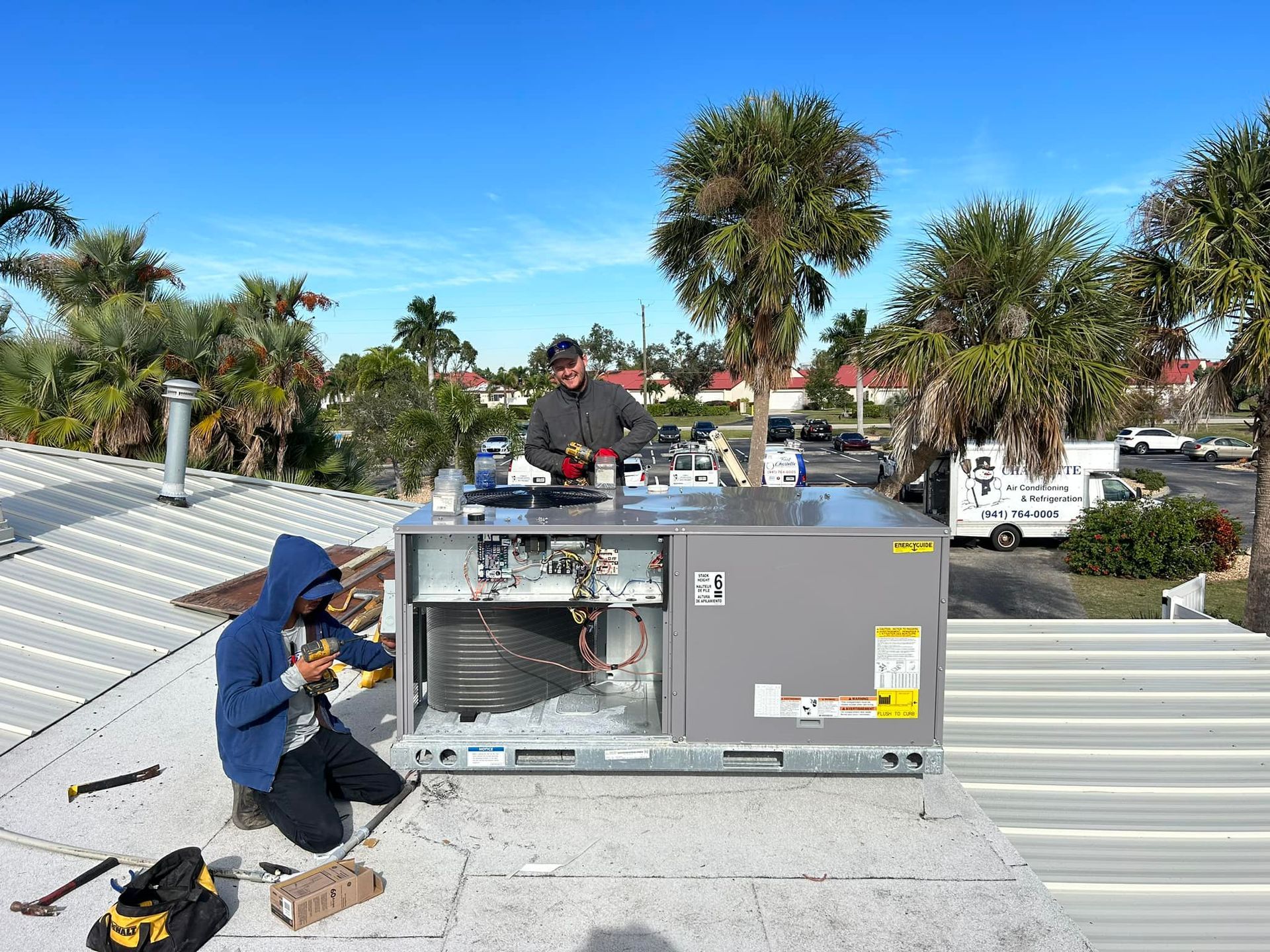Two men are working on an air conditioner on top of a roof.