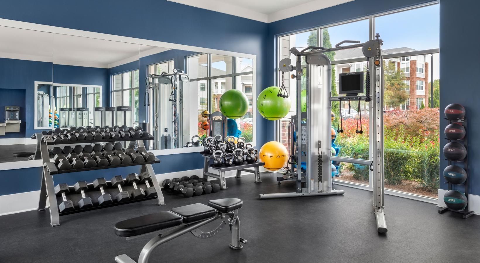 A gym with a lot of dumbbells , a bench , and a large window.