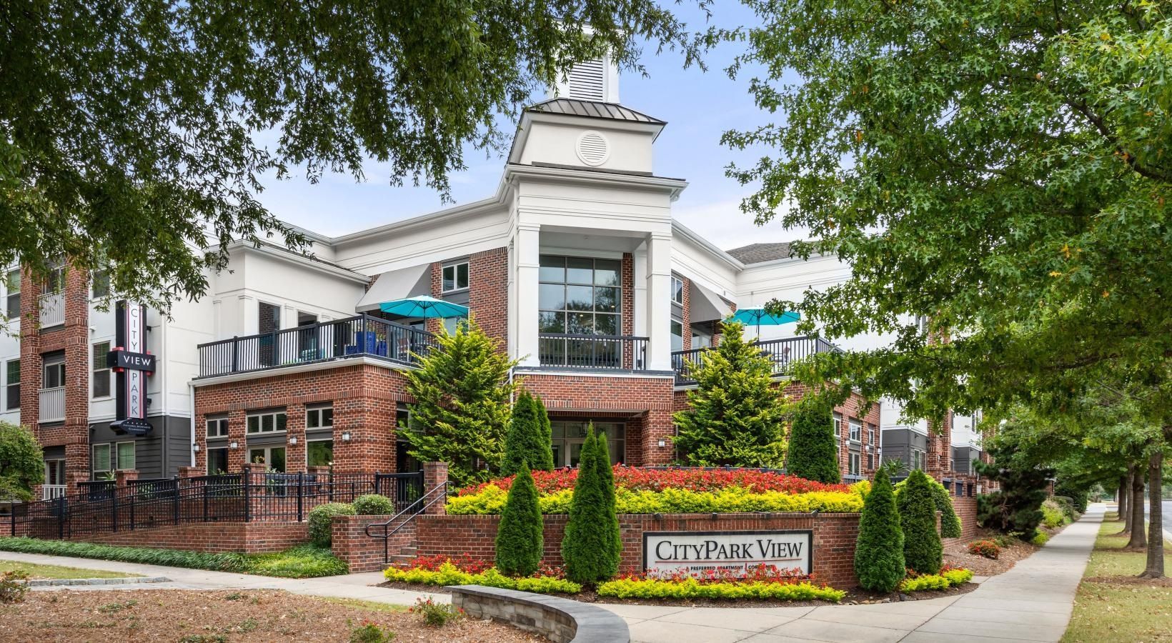 A large brick building with a balcony and umbrellas in front of it.