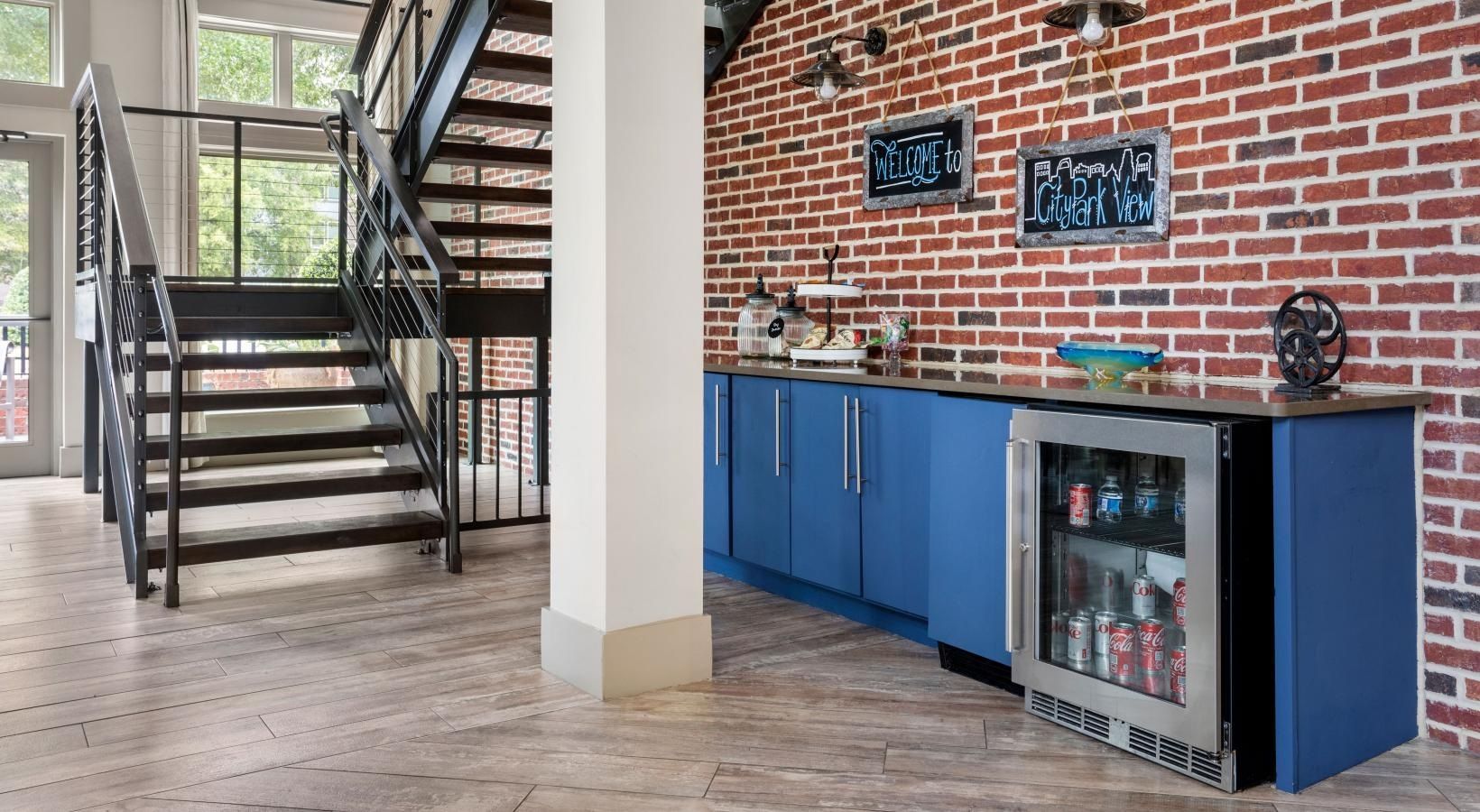 A kitchen with blue cabinets , a refrigerator , a staircase and a brick wall.