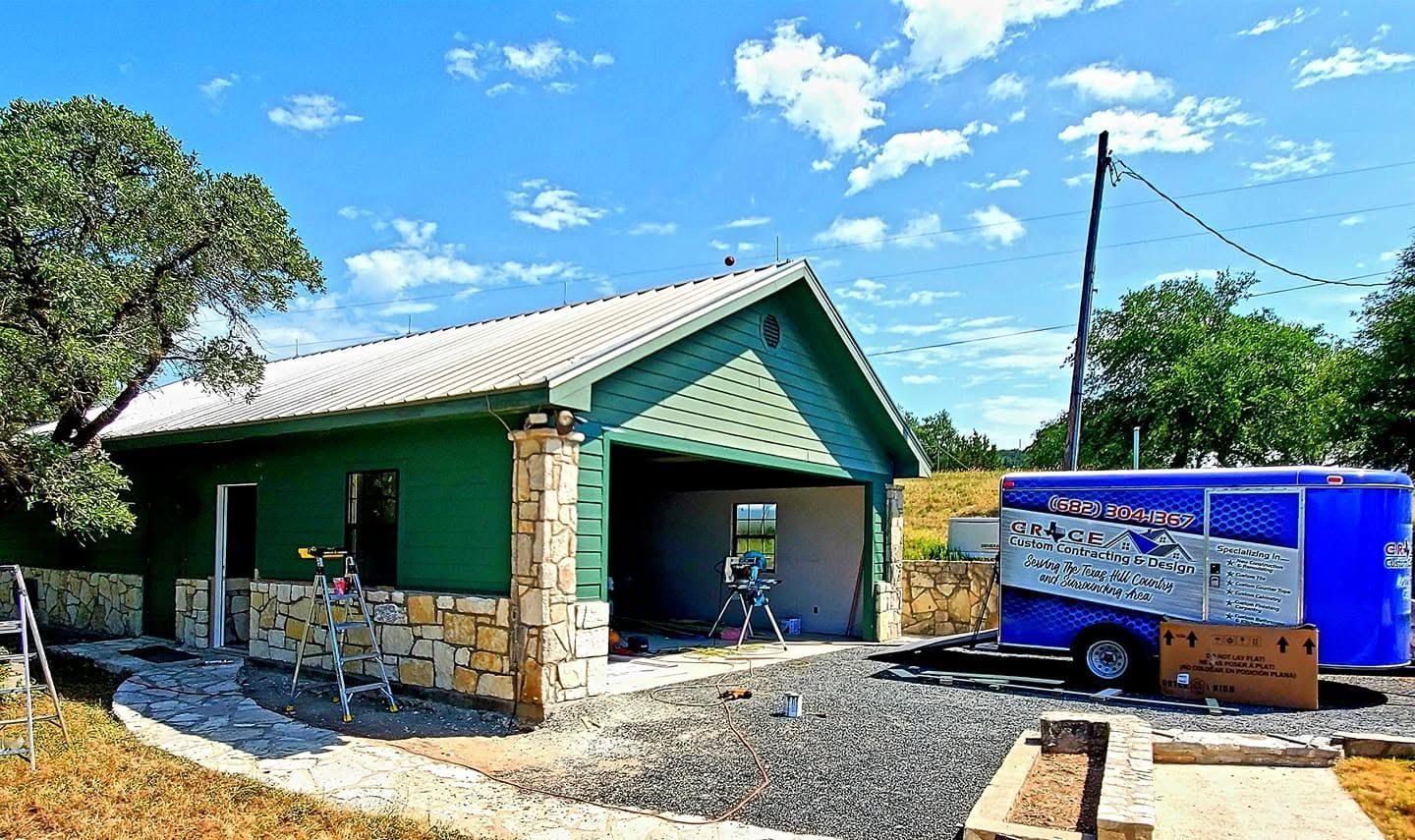 Green house with a metal roof beside a blue trailer under a bright sky