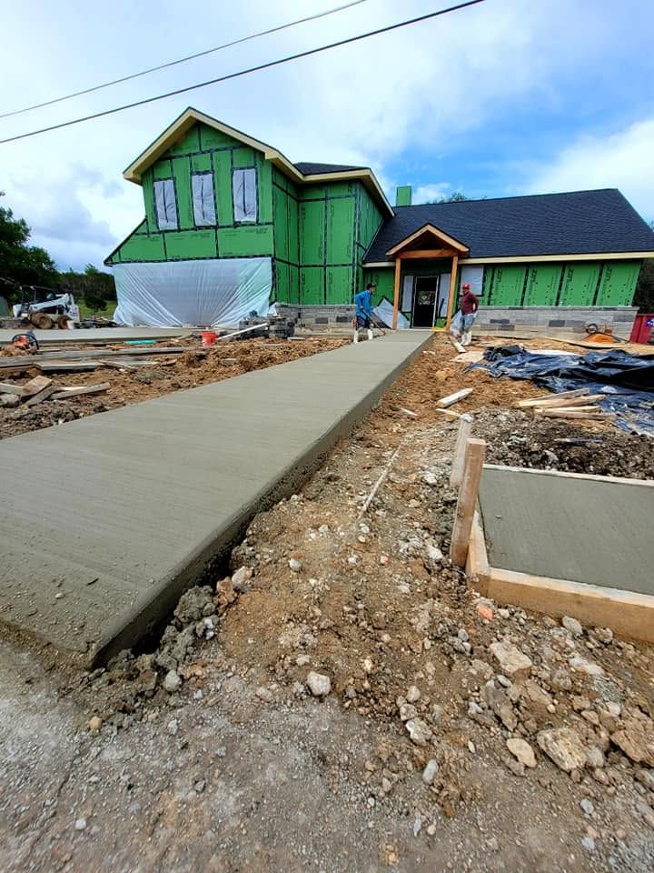Unfinished house with green siding and a concrete walkway under construction, surrounded by dirt and debris