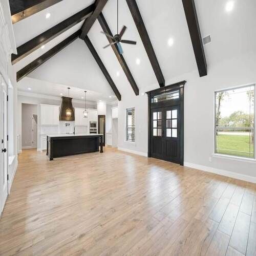 Bright open living room with vaulted ceiling, exposed beams, black kitchen island, and hardwood floors