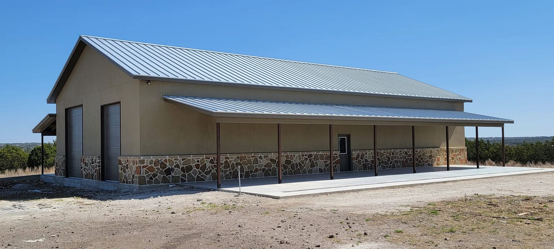 Single-story beige building with a metal roof and covered porch in a dry, open field