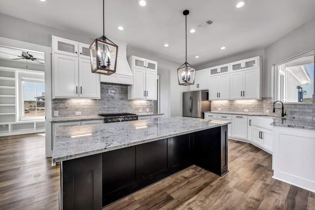 Bright modern kitchen with white cabinets, granite counters, dark island, pendant lights, and wood floors
