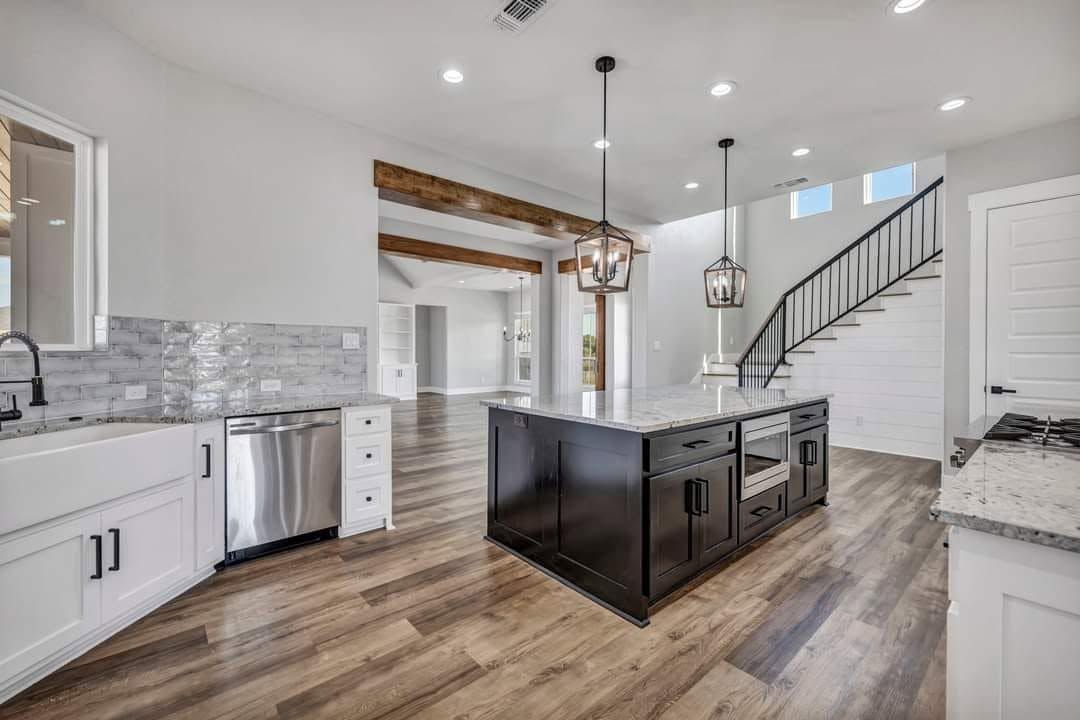 Modern kitchen with island, white cabinets, stainless appliances, wood floors, and staircase in background