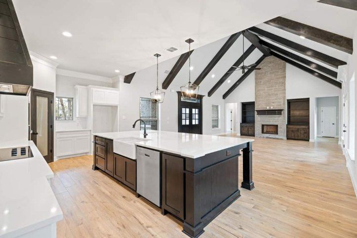 Open-concept kitchen and living room with vaulted black beams, white cabinets, and a large island.