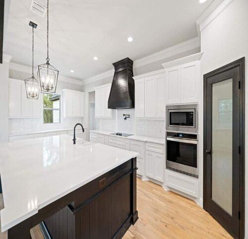 Bright modern white kitchen with island, black accents, built-in oven, and wood floors