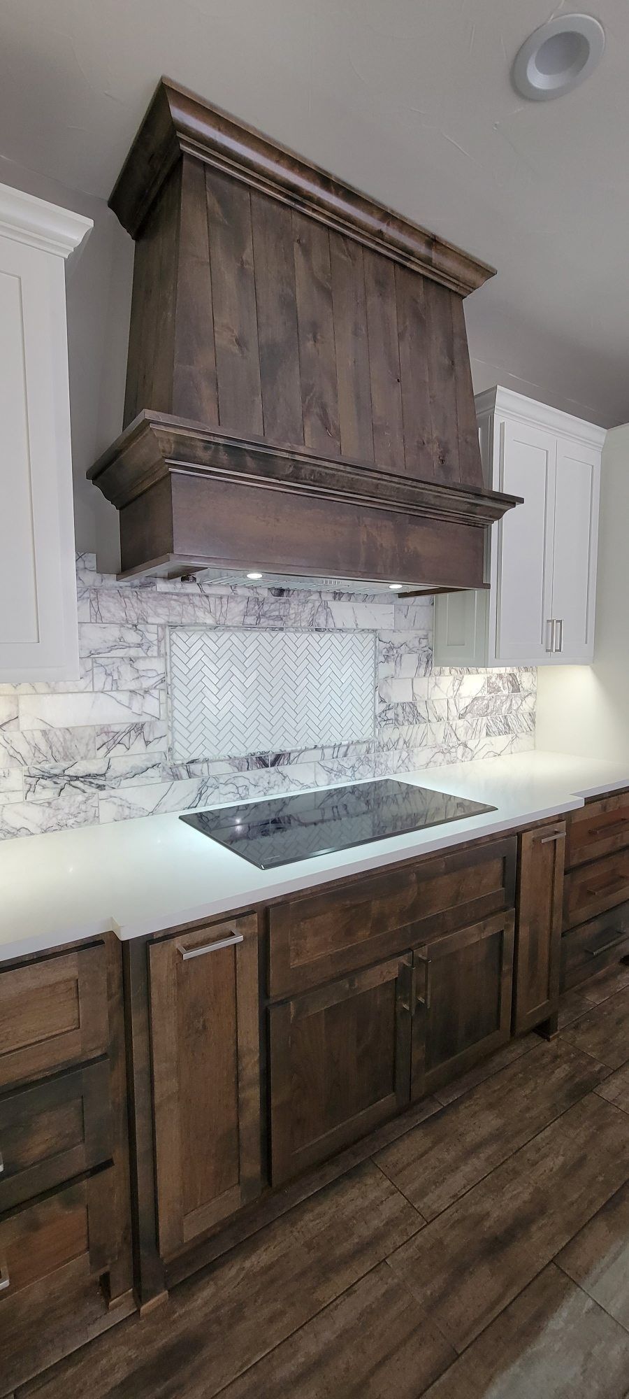Modern kitchen with dark wood cabinets, marble backsplash, and a large wood range hood.
