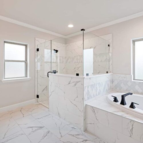 Bright white marble-tiled bathroom with glass shower, soaking tub, and two windows