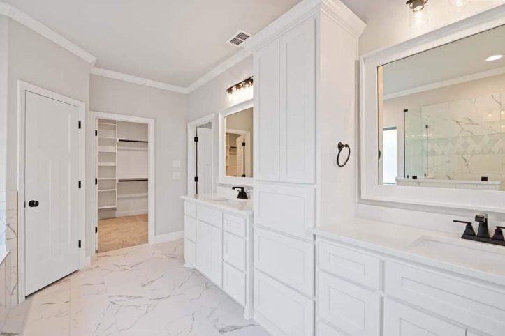 Bright white bathroom vanity area with double sinks, mirrors, and an open walk-in closet.