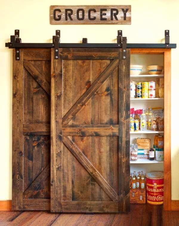Wooden sliding pantry door with a “GROCERY” sign, revealing shelves of canned and jarred food inside.