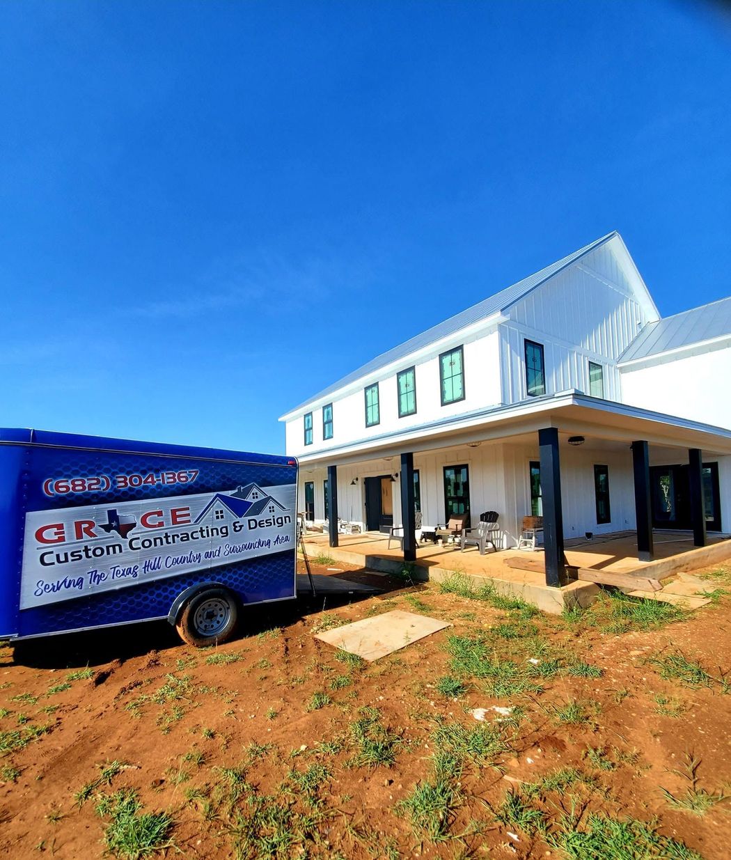 Blue-and-white custom home under construction beside a work truck on a dirt lot under a clear sky