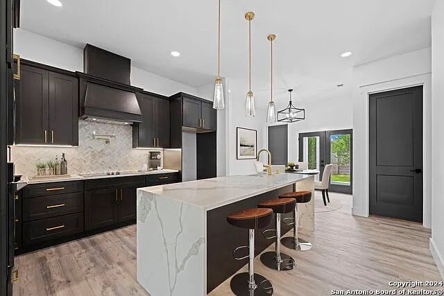Modern kitchen with dark cabinets, marble island, and three stools under pendant lights
