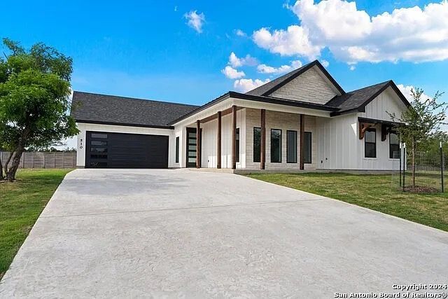 Modern white house with dark roof, covered entry, and a wide concrete driveway under a blue sky