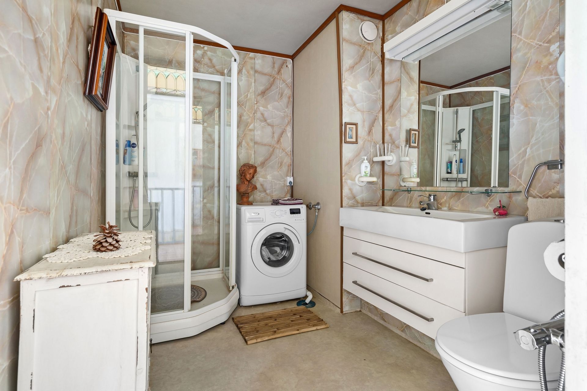 Compact bathroom with shower, white vanity, toilet, and washing machine under a mirrored cabinet