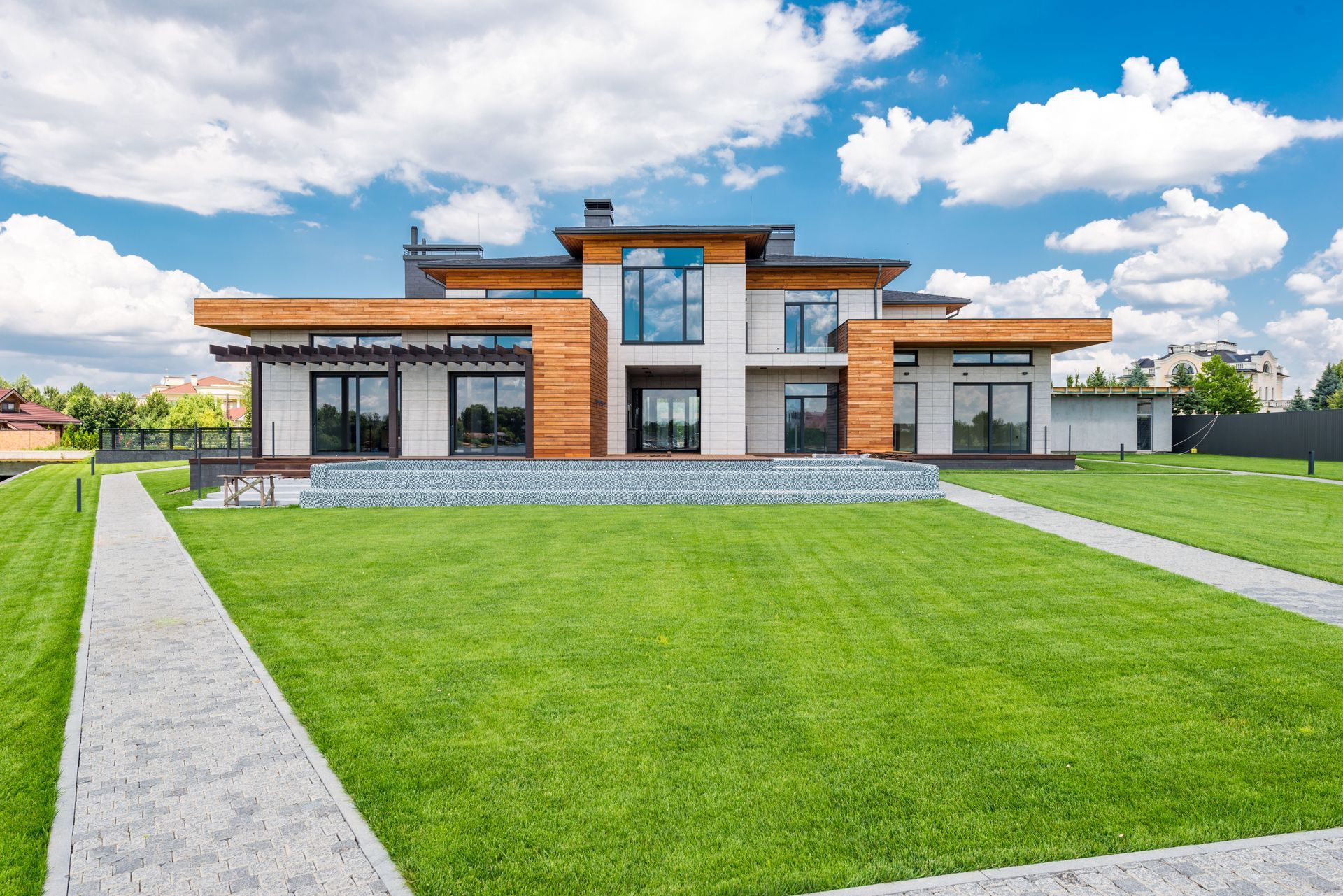 Modern single-story house with large windows, brick accents, and a manicured green lawn under a cloudy sky