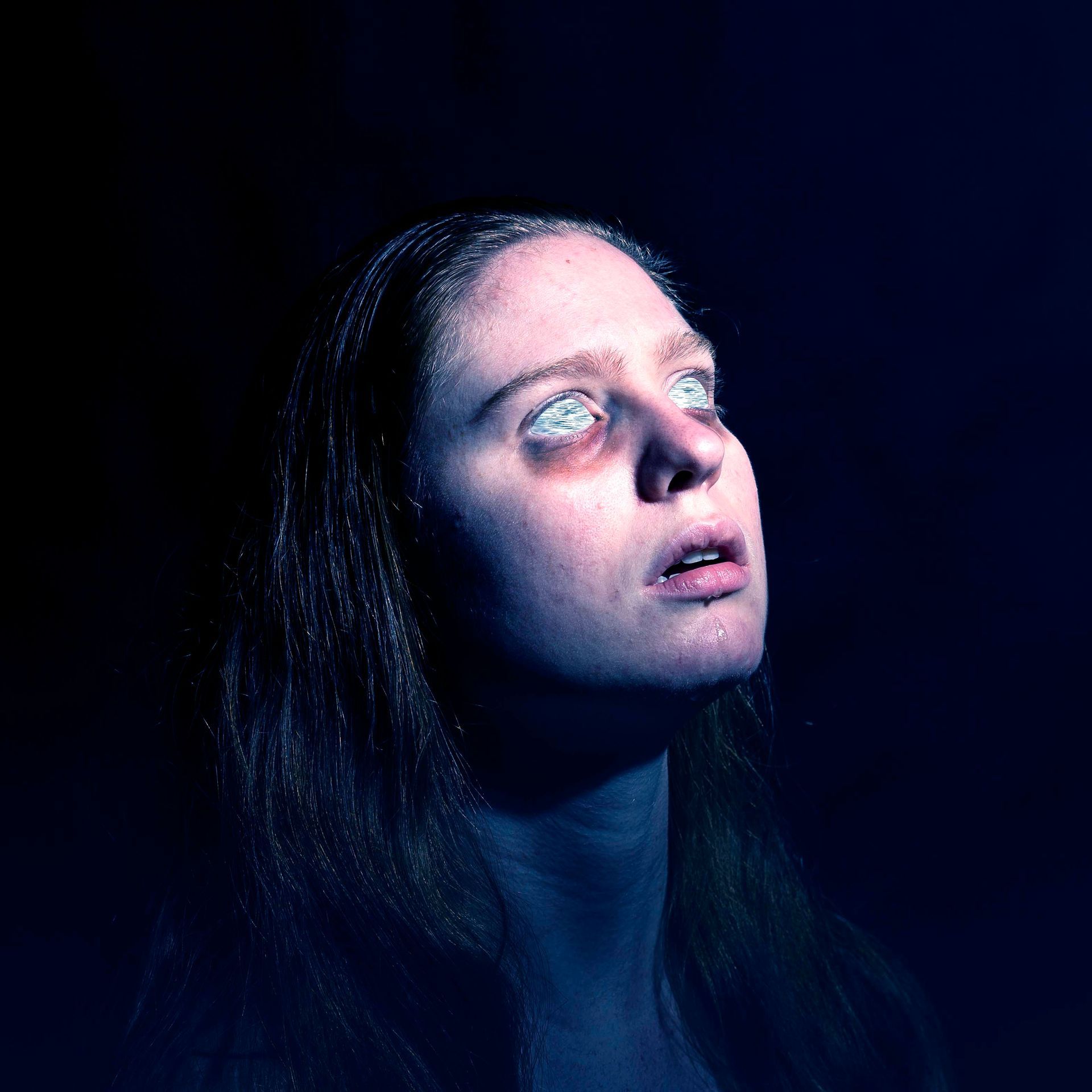 A woman with blue eyes is looking up in the dark.