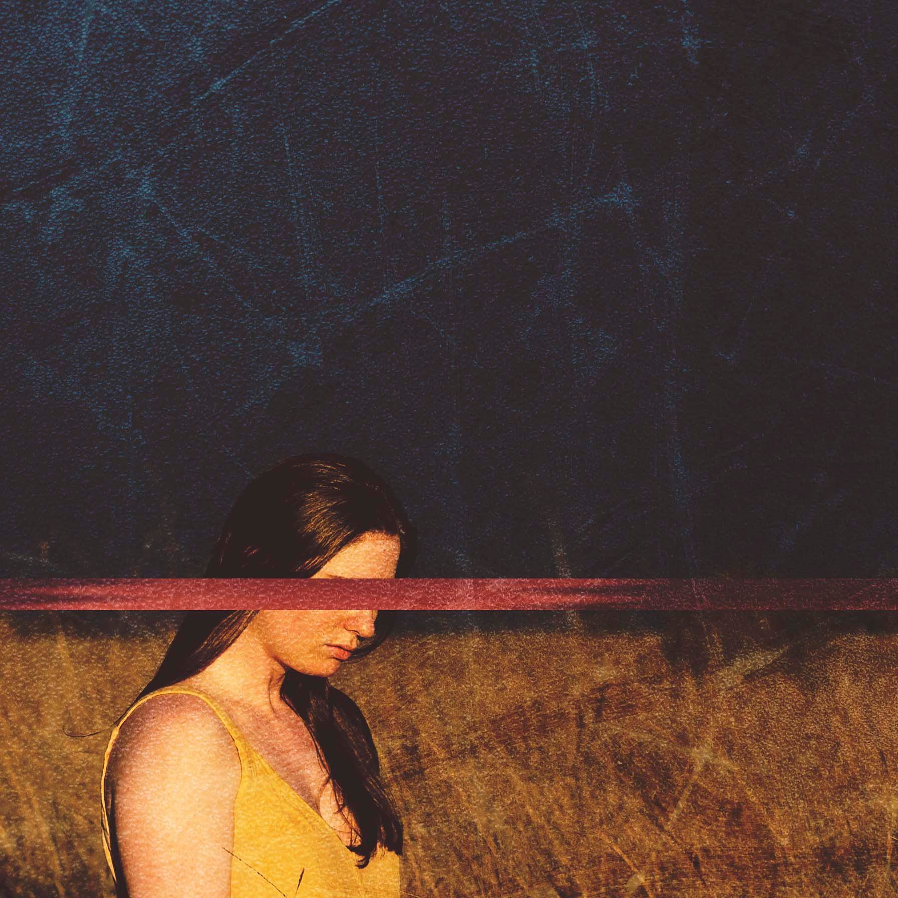 A woman in a yellow dress is standing in a field with a red ribbon covering her face.