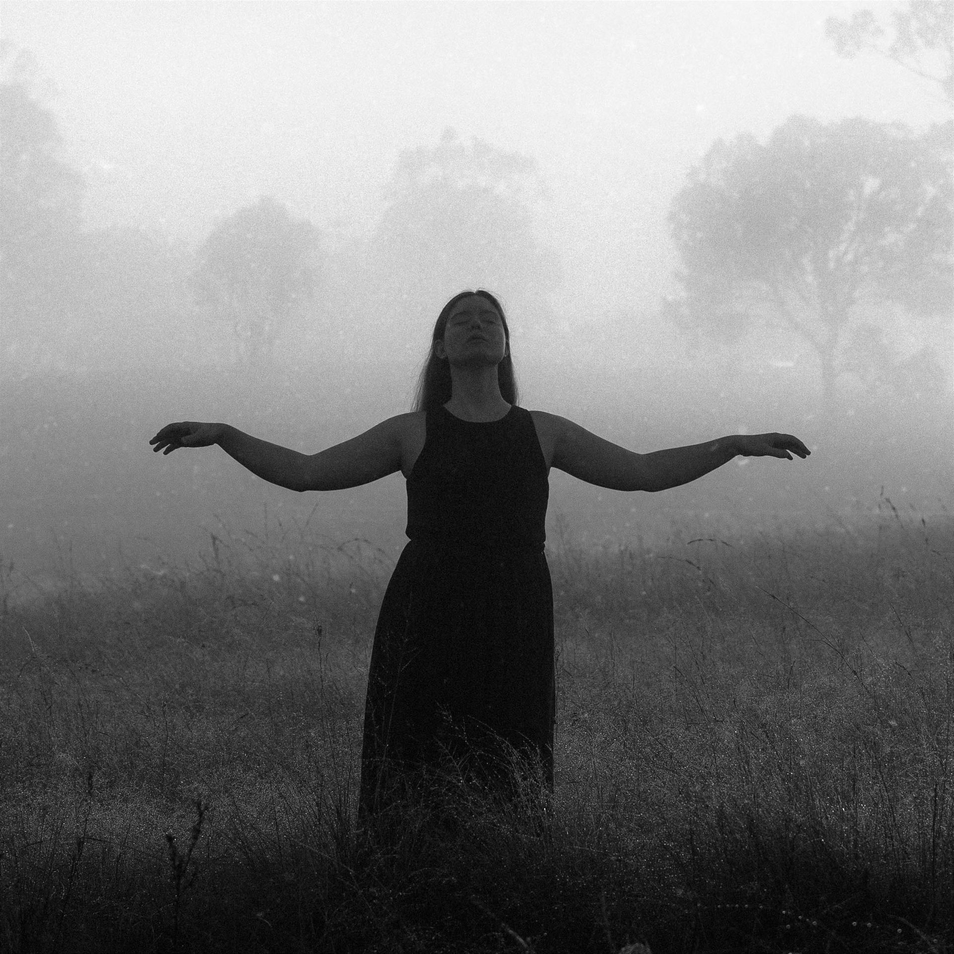 A woman in a black dress is standing in a field with her arms outstretched