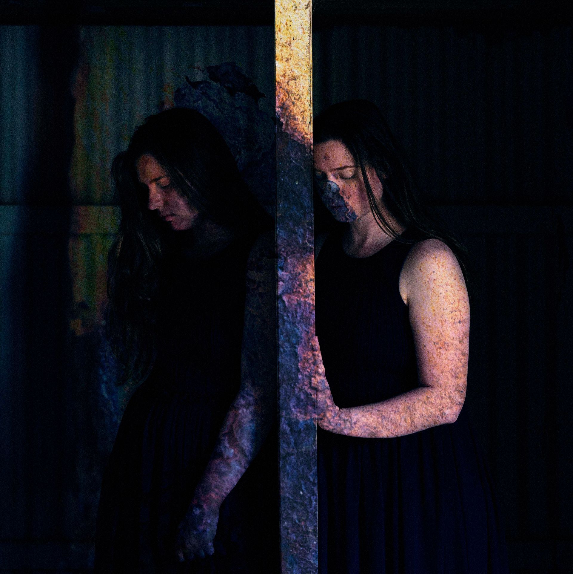 A woman in a black dress is standing next to a pole in a dark room.
