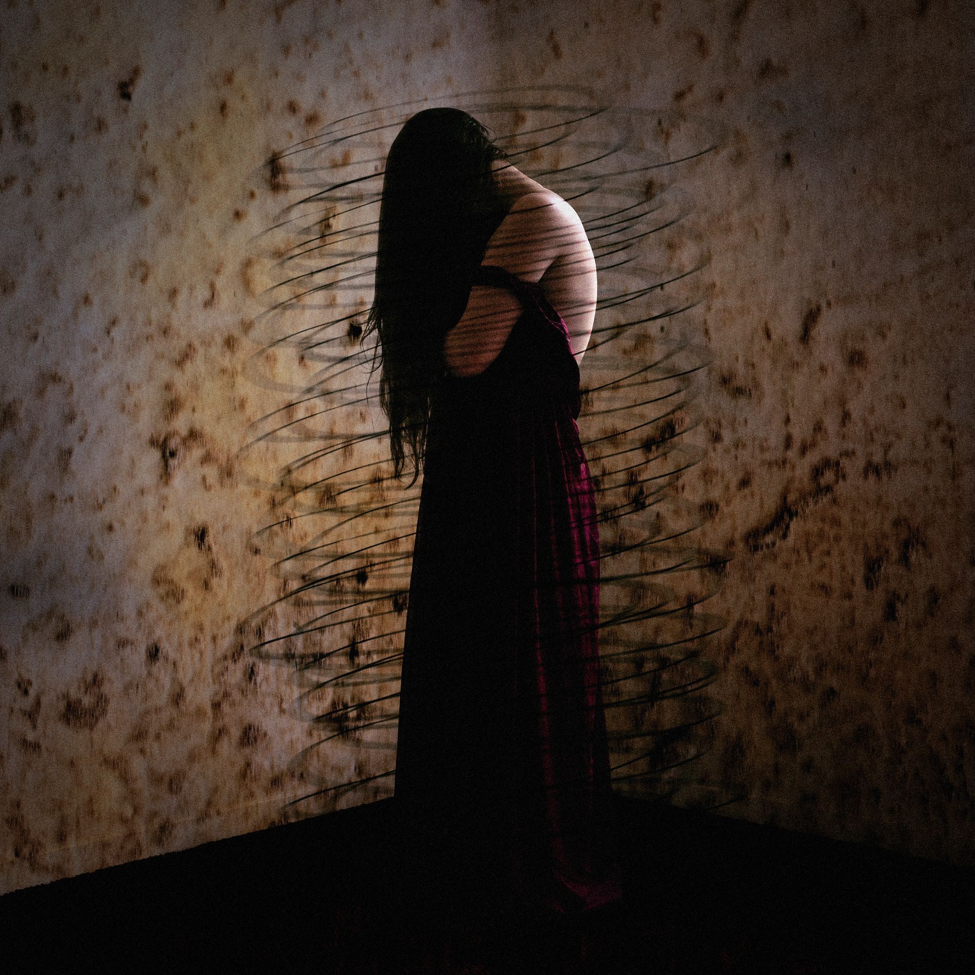 A woman in a long black dress is standing in front of a wall