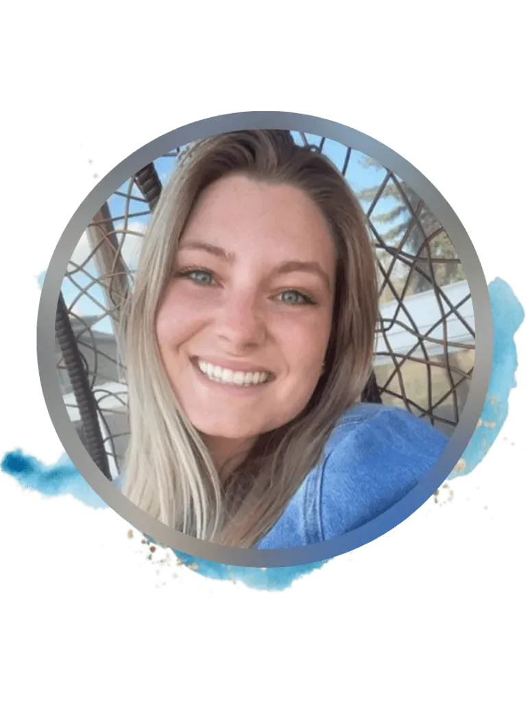 Woman with blonde hair smiling, in a blue denim jacket, seated outdoors.