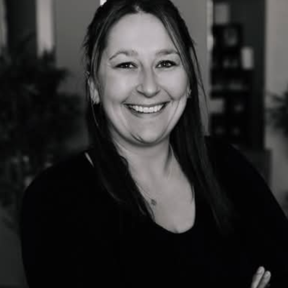 Woman with long hair smiles broadly, arms crossed, wearing a dark top.