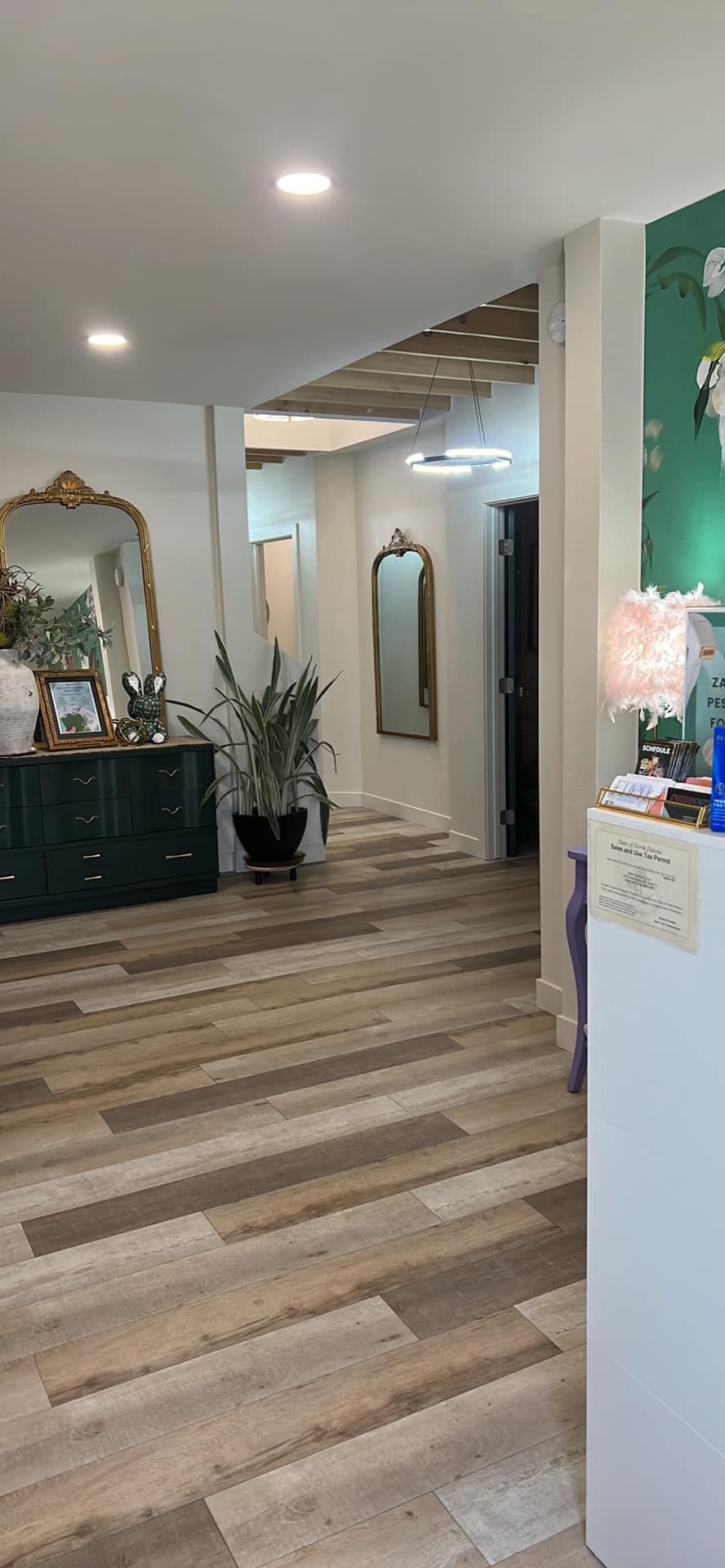 A hallway with wooden floors, a green dresser, and decorative mirrors.