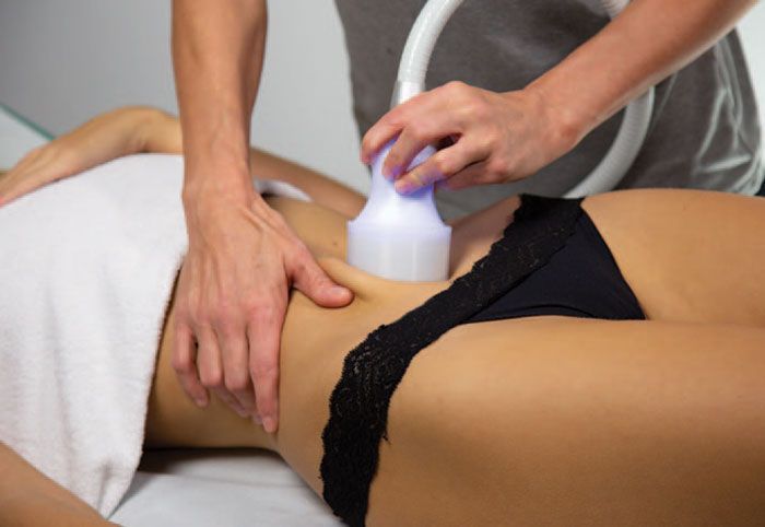 Person receiving body contouring treatment on stomach; a handheld device is used.