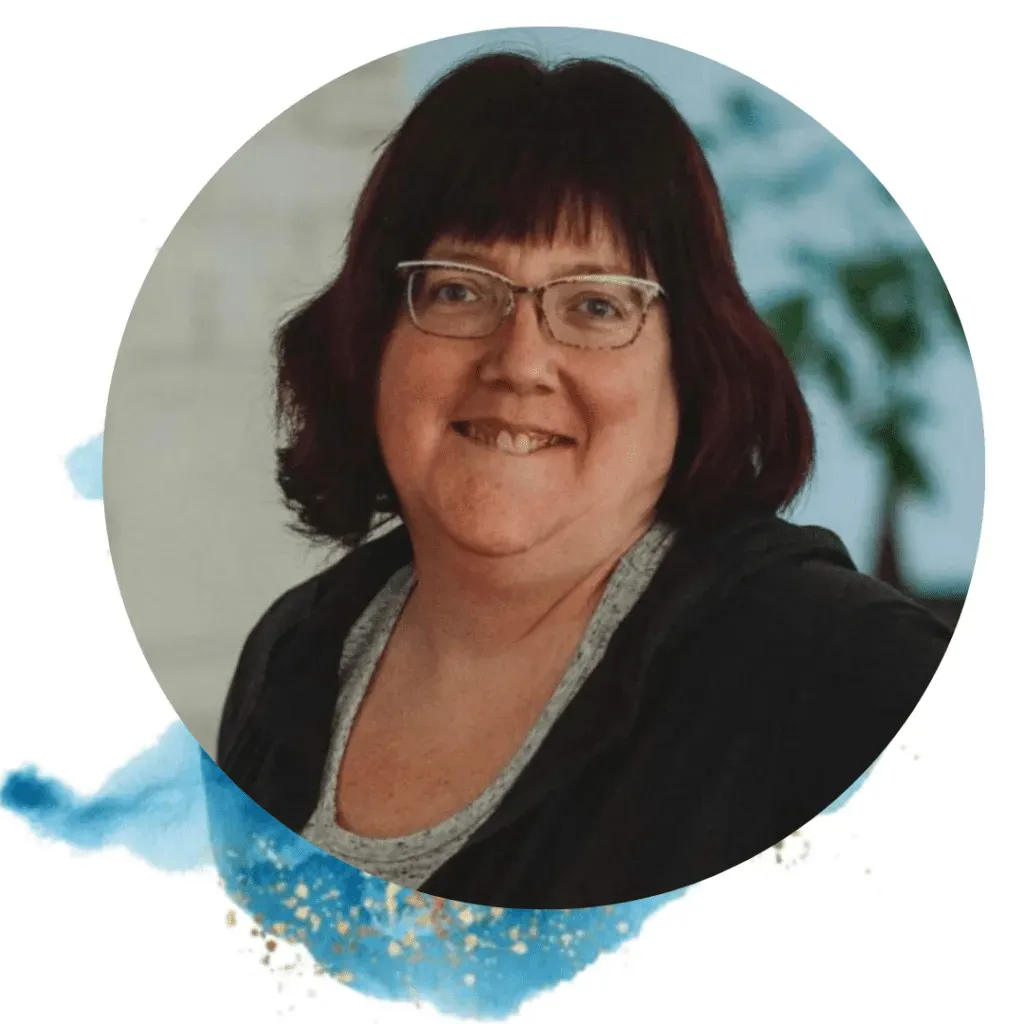 Woman with glasses smiles; dark hair with bangs, in a casual setting.