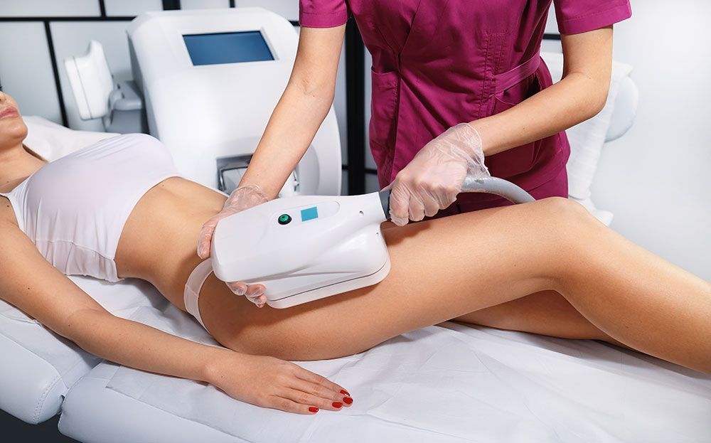 Woman receiving body contouring treatment with a handheld device on her thigh.