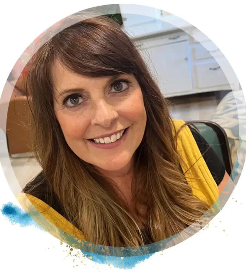 Woman with long brown hair, smiling, wearing a yellow top. Set against a blurred background.